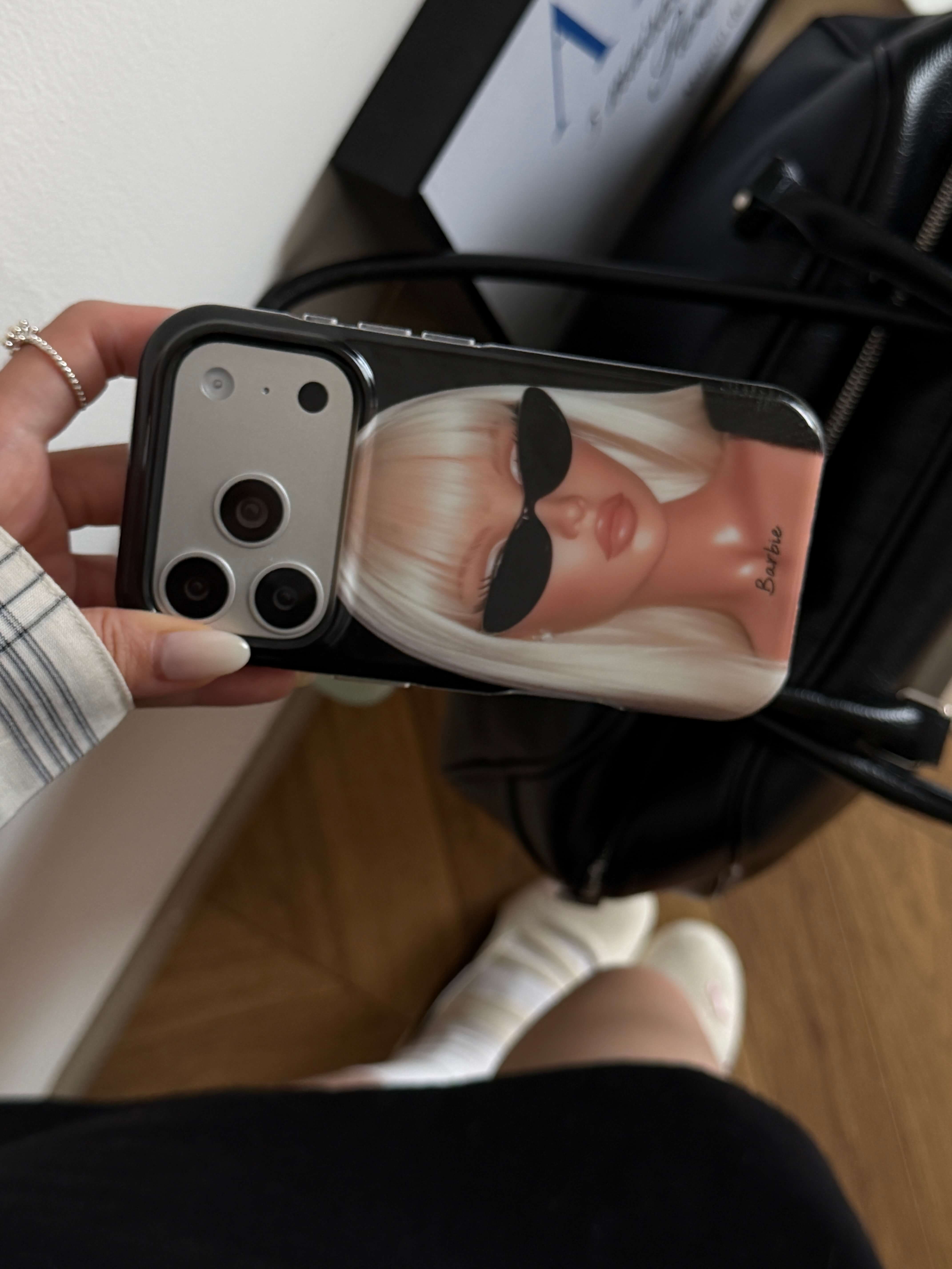 Hand holding a glossy black blonde girl iPhone case near a leather bag.