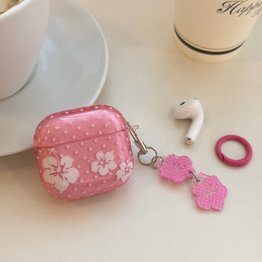 A pink floral polka dot AirPods case lying on a table next to a white wireless earbud and a pink carabiner ring.