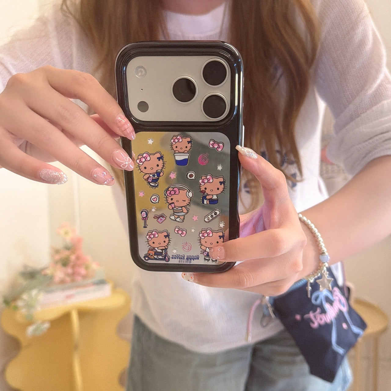 A close-up mirror selfie showing a silver-framed Hello Kitty mirror phone case and beautifully manicured nails.