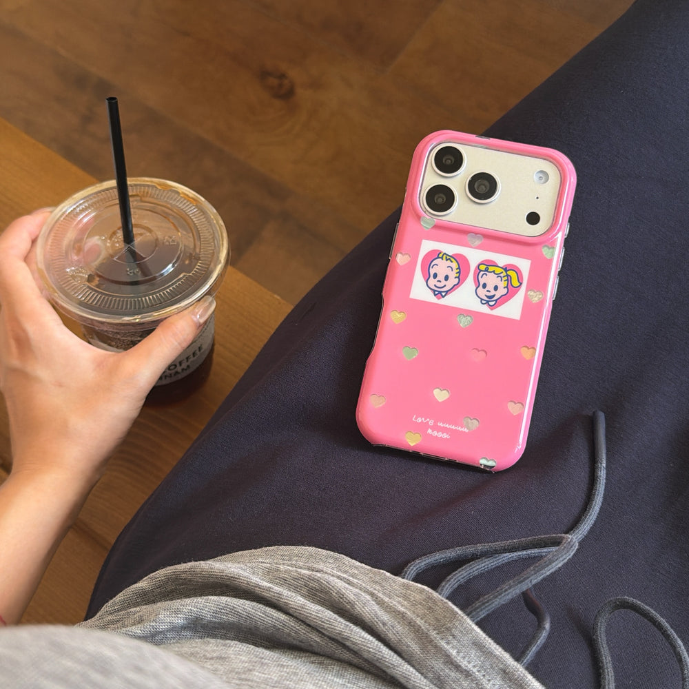 A pink Y2K heart iPhone case resting on a person's lap next to an iced coffee cup.