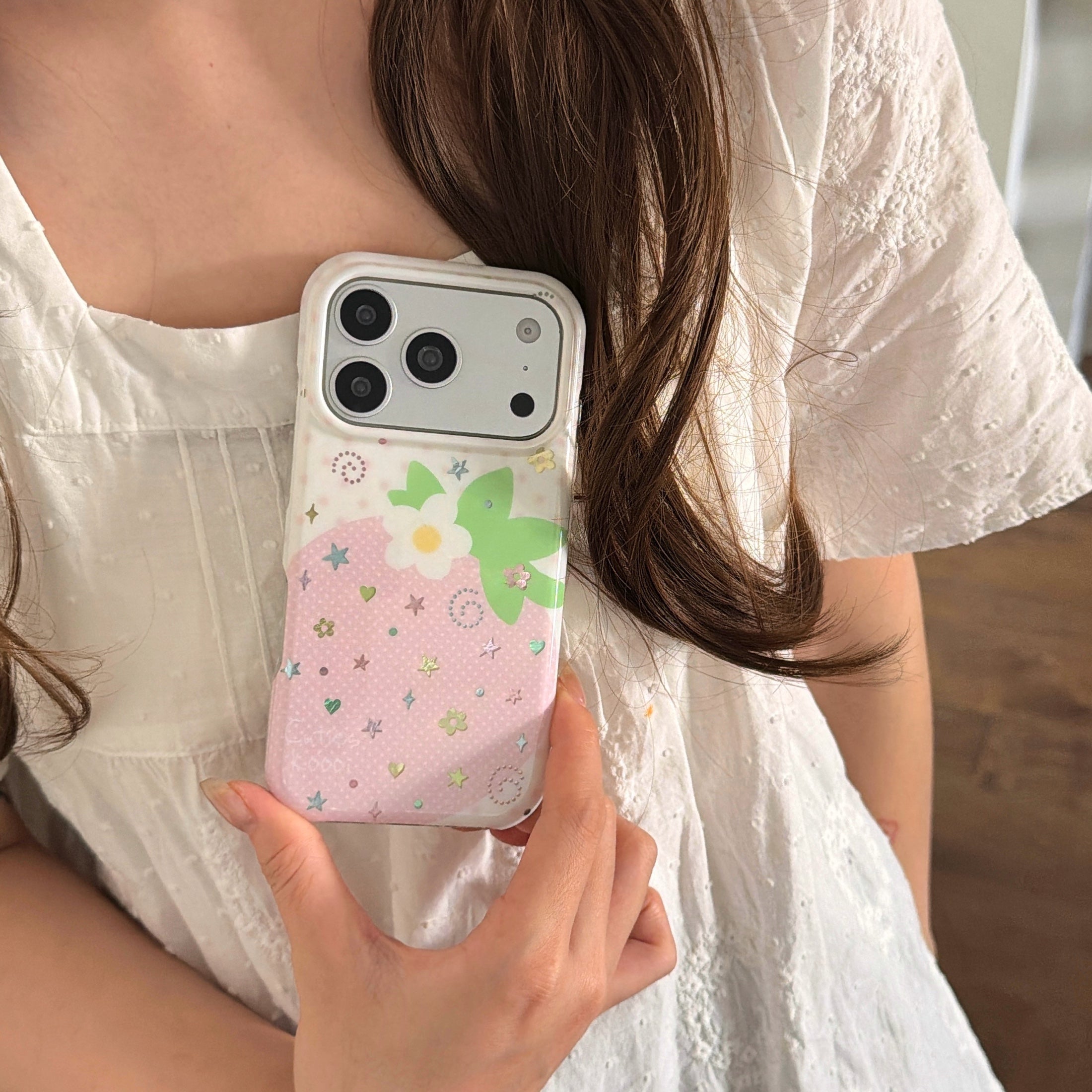 Close-up view of a woman wearing a white summer dress showcasing the back design of a y2k pink strawberry phone case.