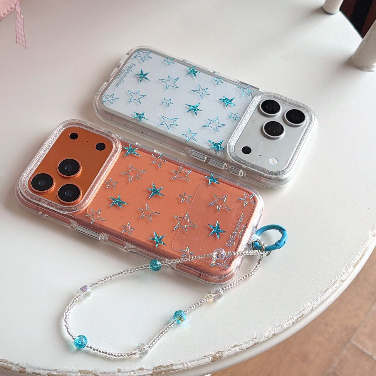 Silver and orange Y2K star phone cases with a beaded wristlet on a white table.