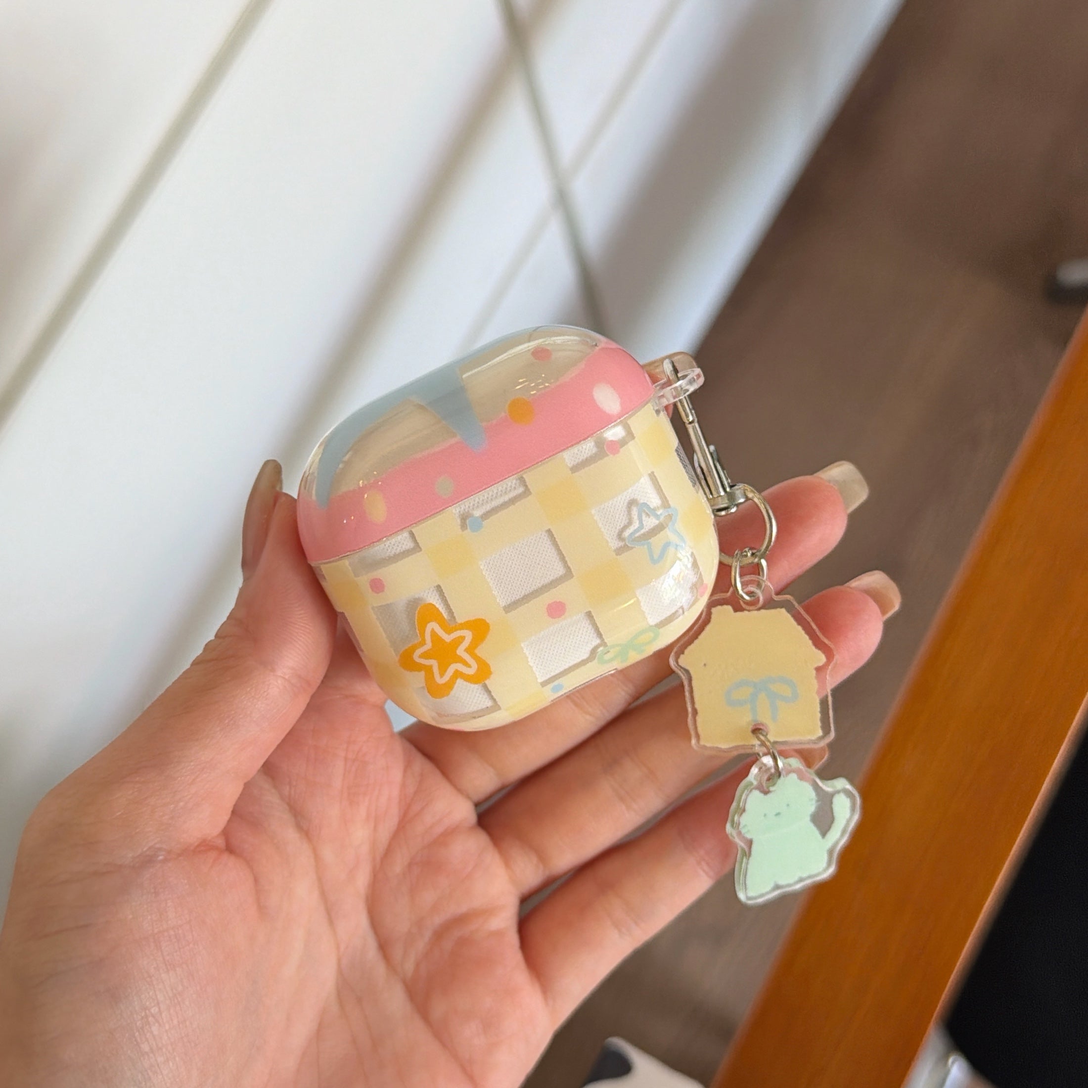 A close-up of a hand holding a yellow check grid pattern AirPods case cover with star graphics.
