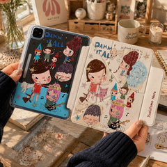 A close-up lifestyle shot of a person in a dark blue sweater holding an open Yoshitomo Nara style aesthetic anime iPad case over a sunlit wooden desk. The case showcases a cream trifold smart cover on the right printed with iconic big-headed grumpy girl illustrations and the text 'Yoshitomo Nara', and a dark matching back panel on the left. The cozy background features warm ambient sunlight, a glass vase of orange roses, a Matisse art print, and vintage stationery.