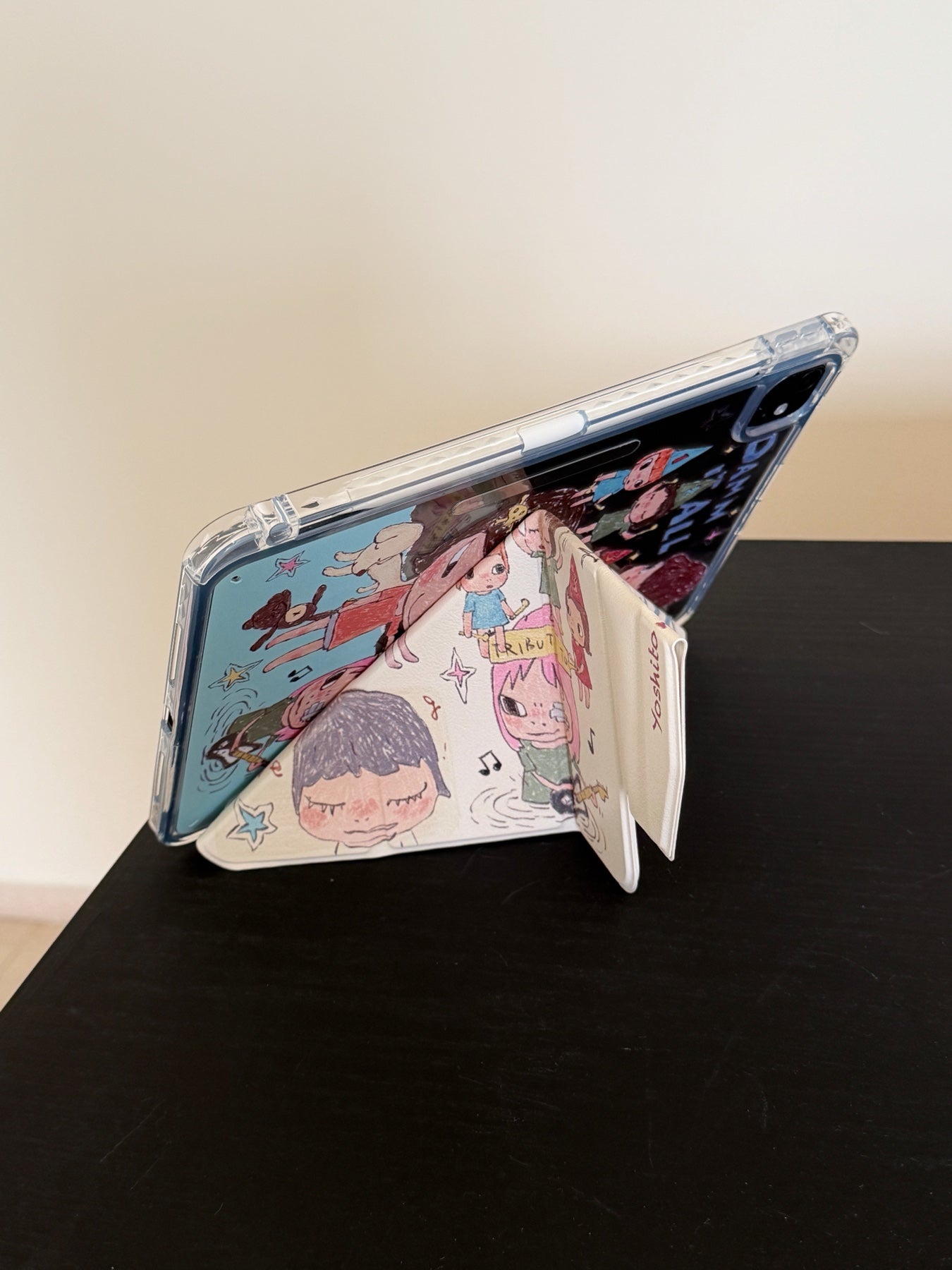 Rear angle view of a Yoshitomo Nara iPad case showing how the magnetic smart cover folds into a secure Y-shaped origami kickstand on a black tabletop.