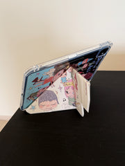 Rear angle view of a Yoshitomo Nara iPad case showing how the magnetic smart cover folds into a secure Y-shaped origami kickstand on a black tabletop.