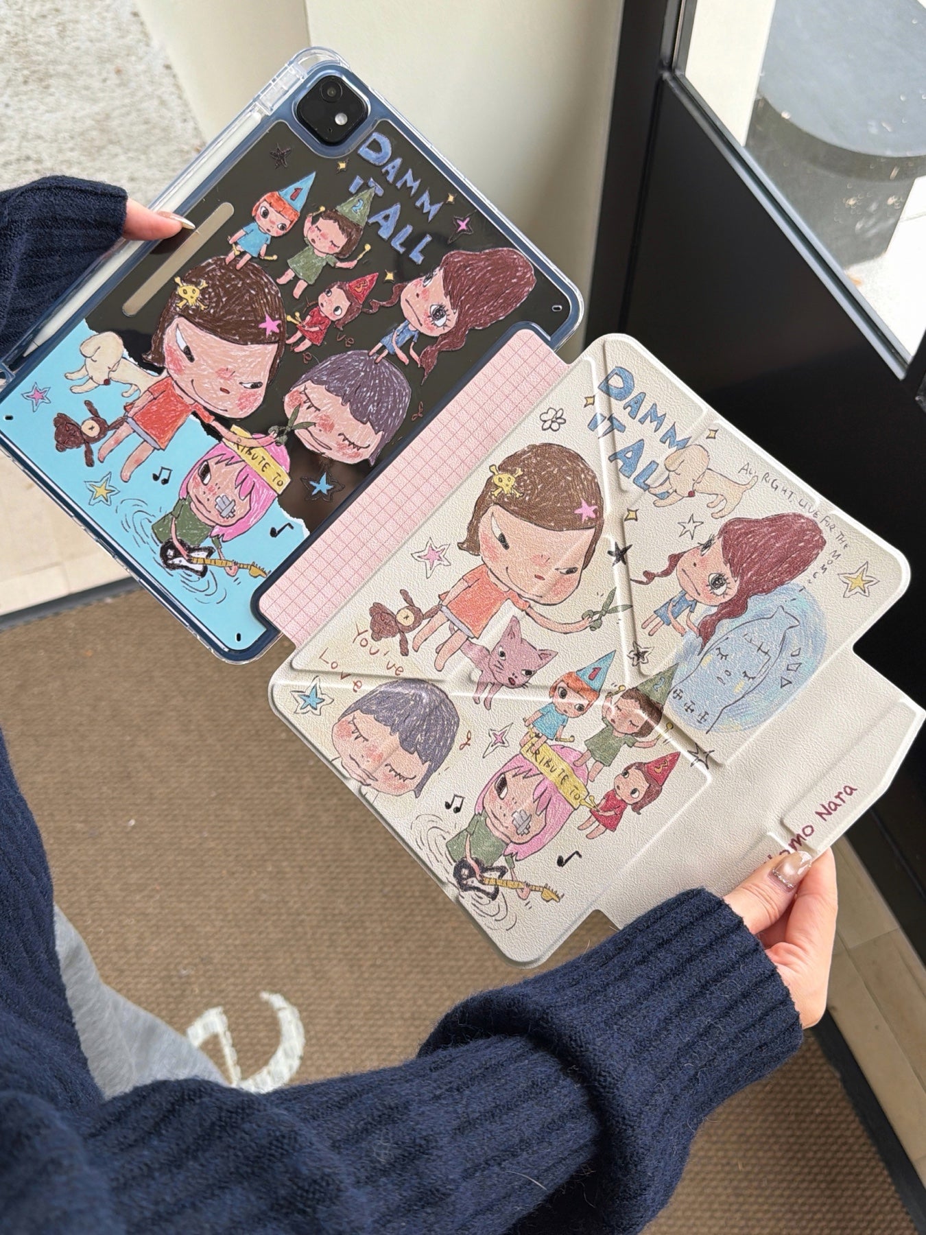 Full view of an opened Yoshitomo Nara iPad case showing the clear protective back shell with colorful cartoon illustrations and the textured front cover.