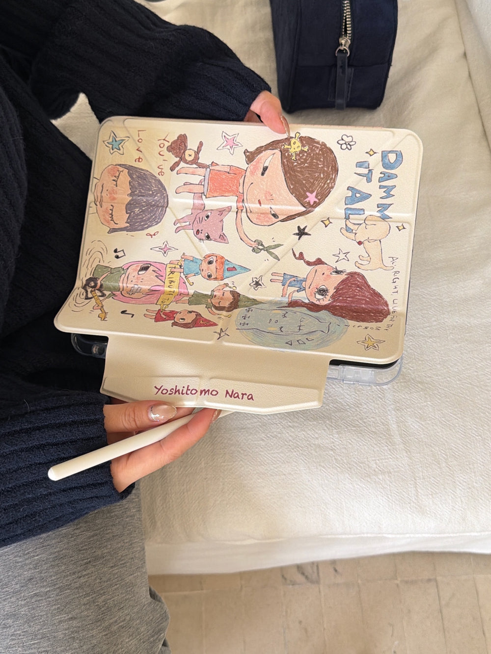 Aesthetic Yoshitomo Nara iPad case details showing the white magnetic closure flap with the artist's name printed on it and a hand holding a stylus.